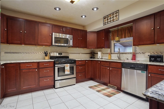 kitchen with a textured ceiling, light stone countertops, sink, and stainless steel appliances