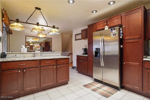 kitchen with hanging light fixtures, light stone countertops, stainless steel fridge, and light tile patterned floors