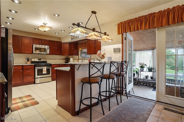 kitchen with a breakfast bar, stainless steel appliances, light tile patterned floors, decorative light fixtures, and light stone countertops