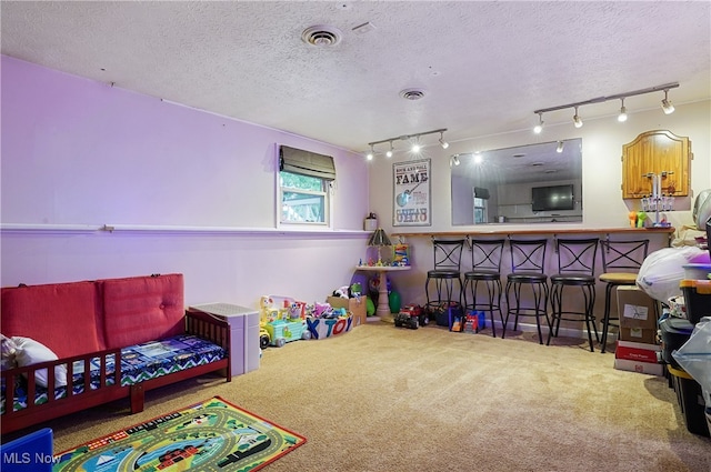 playroom with a textured ceiling, carpet, bar area, and rail lighting