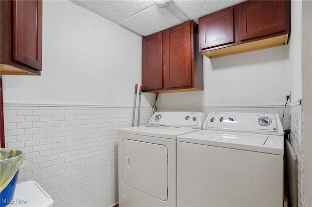 clothes washing area featuring a textured ceiling, tile walls, separate washer and dryer, and cabinets