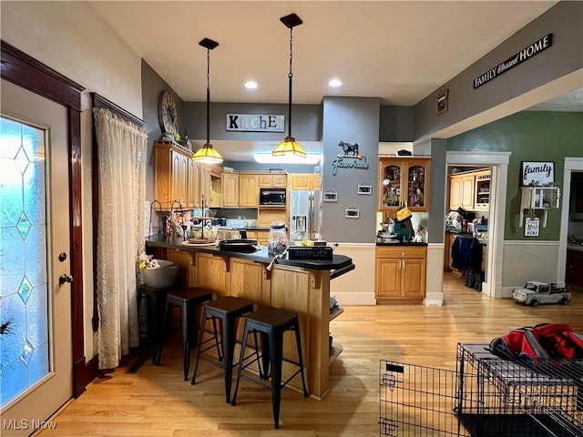 kitchen with a breakfast bar, stainless steel fridge, light hardwood / wood-style floors, and black microwave