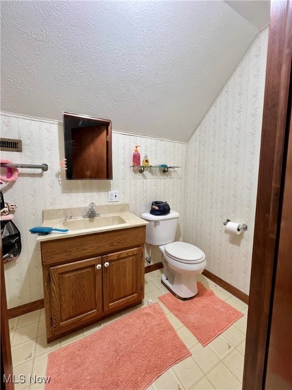 bathroom featuring a textured ceiling, lofted ceiling, vanity, and toilet