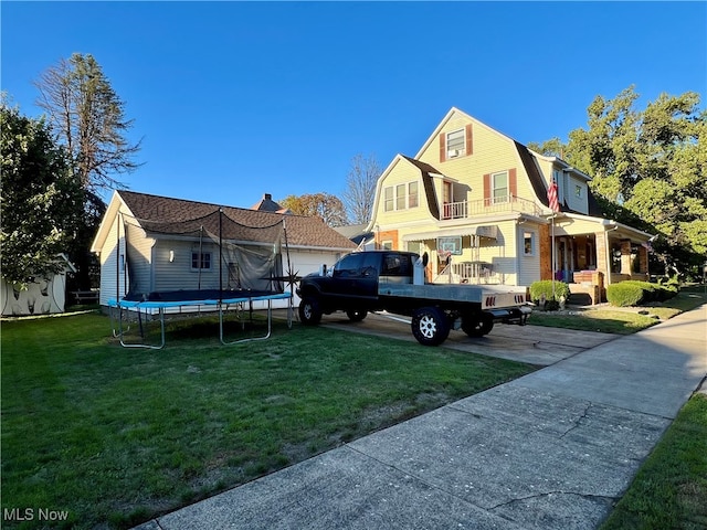 rear view of house featuring a balcony, a trampoline, and a yard