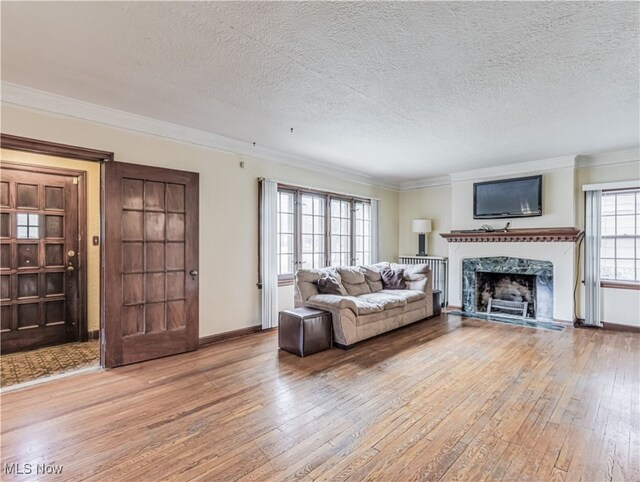 living room with a textured ceiling, light wood-type flooring, a fireplace, and crown molding