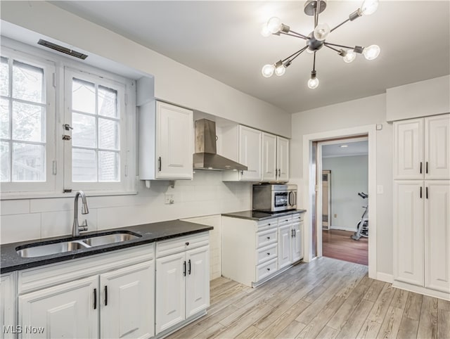 kitchen with wall chimney exhaust hood, white cabinets, light hardwood / wood-style flooring, and sink