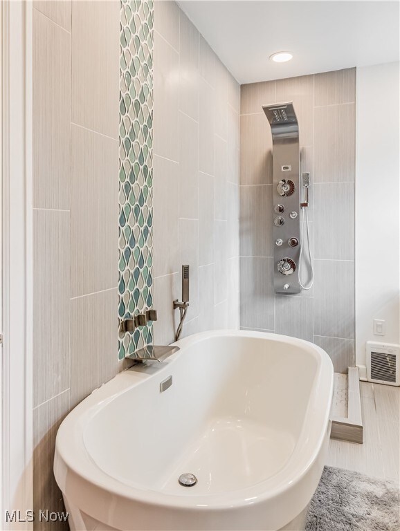 bathroom with a tub to relax in and tile walls