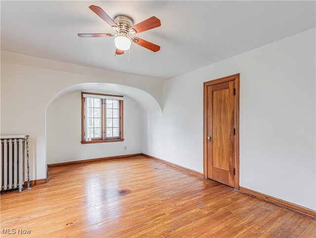 unfurnished room featuring light wood-type flooring, ceiling fan, and radiator heating unit