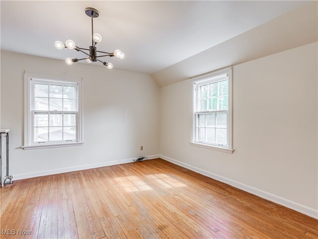 spare room with a notable chandelier, hardwood / wood-style floors, and a wealth of natural light