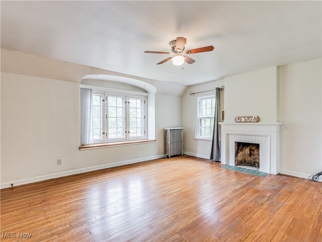 unfurnished living room with a brick fireplace, light hardwood / wood-style flooring, radiator heating unit, and lofted ceiling