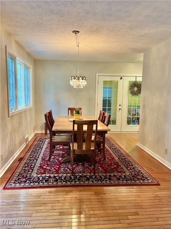 dining space with wood-type flooring, a textured ceiling, french doors, and a notable chandelier