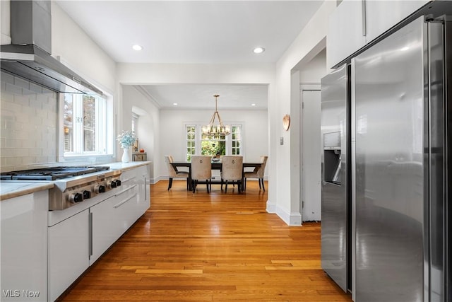 kitchen with light wood-type flooring, backsplash, white cabinetry, stainless steel appliances, and wall chimney range hood