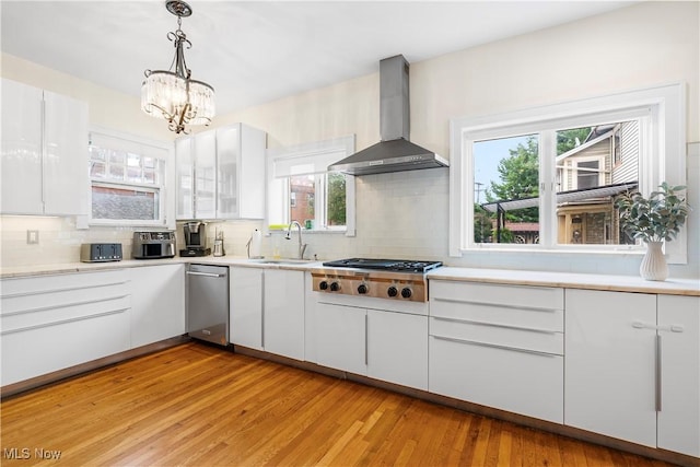 kitchen featuring stainless steel gas cooktop, white cabinets, wall chimney range hood, and a sink