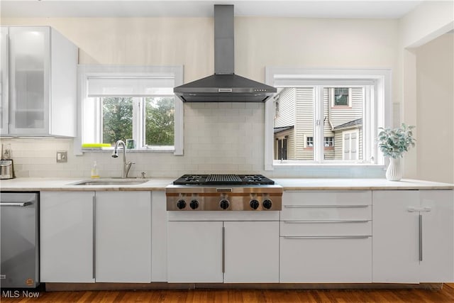 kitchen with light countertops, appliances with stainless steel finishes, white cabinets, wall chimney exhaust hood, and a sink