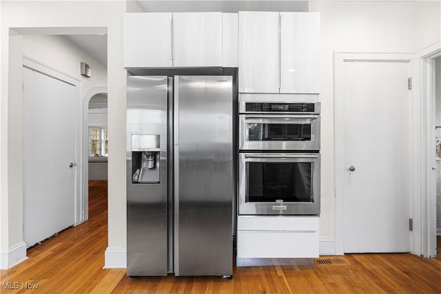 kitchen with arched walkways, white cabinets, stainless steel appliances, and light wood-style floors