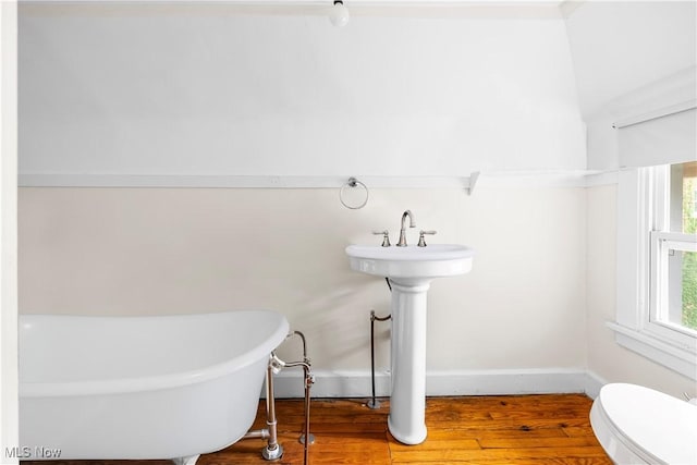 bathroom with toilet, wood finished floors, baseboards, and a freestanding bath