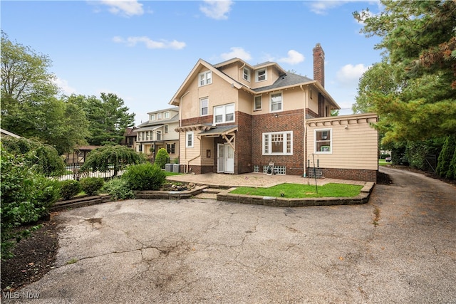 view of front of home with a patio, central AC unit, fence, stucco siding, and a chimney