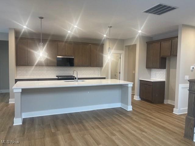 kitchen featuring backsplash, dark wood-type flooring, sink, pendant lighting, and a center island with sink