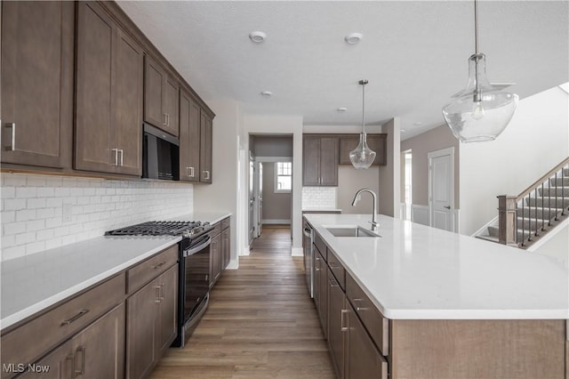 kitchen featuring sink, hanging light fixtures, hardwood / wood-style flooring, stainless steel appliances, and a kitchen island with sink