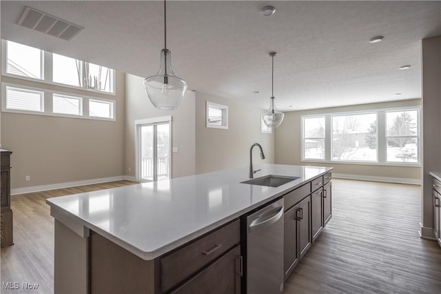 kitchen with hanging light fixtures, dishwasher, sink, and a center island with sink