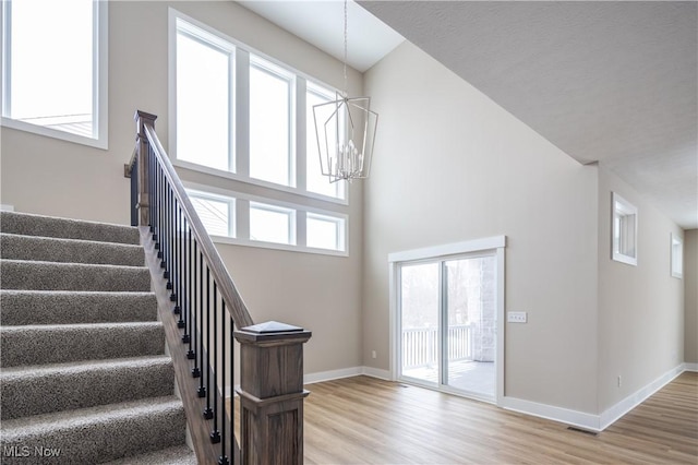 stairs with hardwood / wood-style flooring, plenty of natural light, a chandelier, and a high ceiling