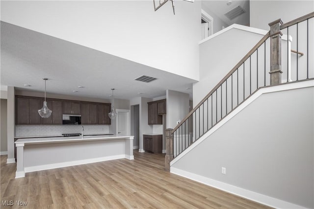 kitchen featuring a towering ceiling, a kitchen breakfast bar, decorative backsplash, dark brown cabinetry, and light wood-type flooring