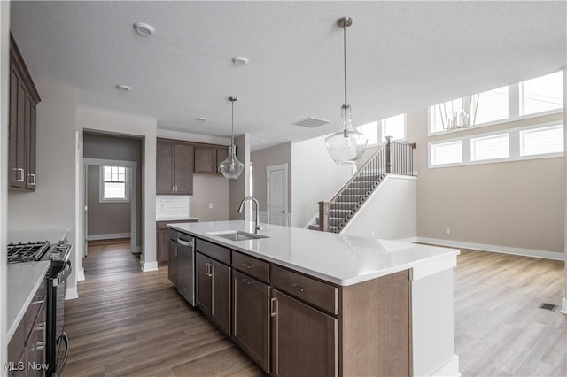 kitchen with sink, dark brown cabinets, appliances with stainless steel finishes, an island with sink, and hardwood / wood-style flooring