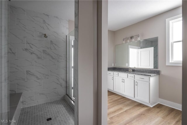 bathroom featuring hardwood / wood-style flooring, vanity, a healthy amount of sunlight, and a tile shower