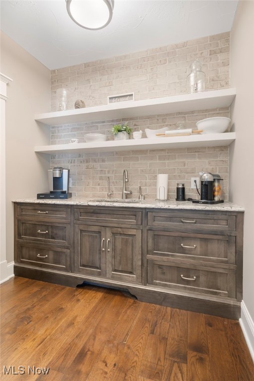 bar featuring dark brown cabinetry, sink, dark wood-type flooring, and decorative backsplash