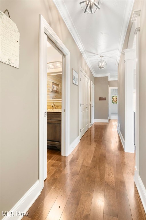 hallway with ornamental molding, baseboards, an inviting chandelier, and wood finished floors