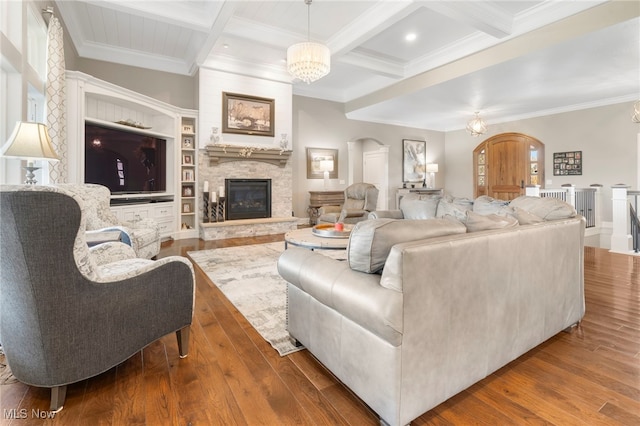 living room featuring ornamental molding, wood-type flooring, beam ceiling, and a stone fireplace