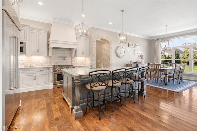 kitchen featuring white cabinets, light stone countertops, wood-type flooring, a center island with sink, and high end range