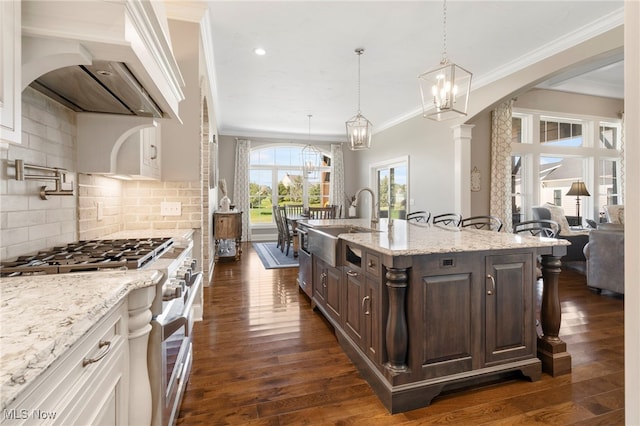 kitchen with stainless steel range, custom exhaust hood, a sink, an island with sink, and dark brown cabinets