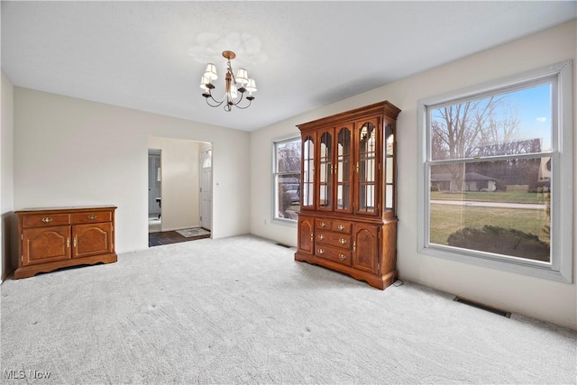 carpeted empty room with plenty of natural light and a chandelier