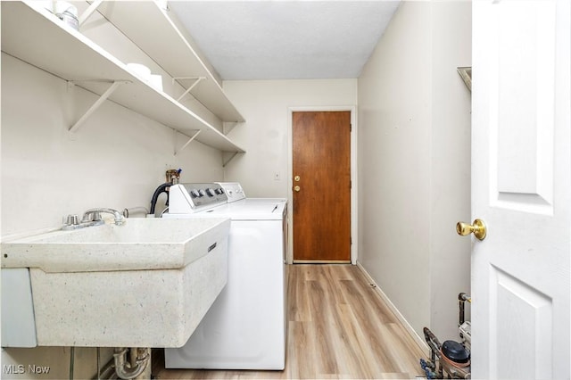 clothes washing area featuring separate washer and dryer, sink, and light wood-type flooring