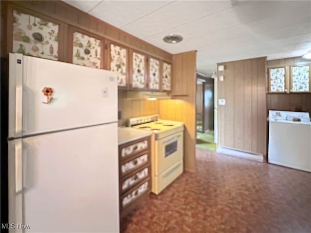 kitchen featuring carpet, white appliances, wood walls, and washer / dryer