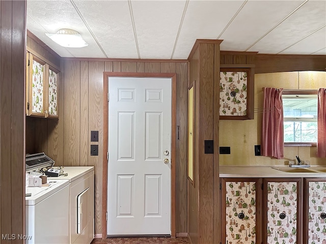 clothes washing area featuring cabinets, wooden walls, washer and clothes dryer, and sink