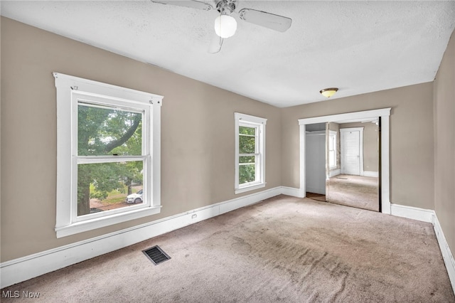 carpeted empty room featuring ceiling fan, a textured ceiling, and a healthy amount of sunlight