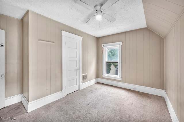 bonus room with a textured ceiling, vaulted ceiling, wooden walls, carpet, and ceiling fan