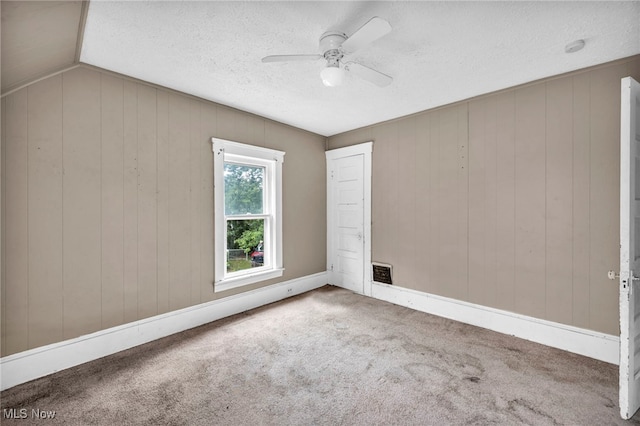 carpeted empty room featuring vaulted ceiling, ceiling fan, wood walls, and a textured ceiling