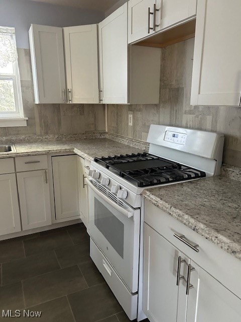 kitchen with light stone counters, decorative backsplash, white gas range, and white cabinetry