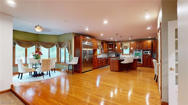 kitchen with backsplash, a breakfast bar area, stainless steel appliances, a center island, and light hardwood / wood-style flooring