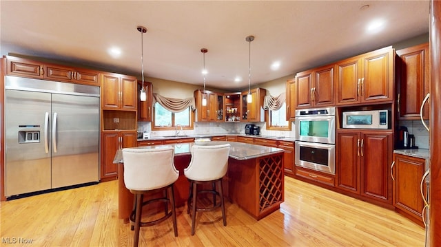 kitchen with light wood-type flooring, a kitchen bar, a center island, and built in appliances