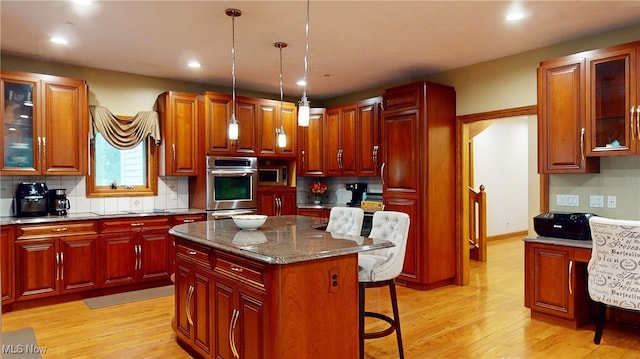 kitchen with a kitchen breakfast bar, a center island, light hardwood / wood-style flooring, decorative light fixtures, and dark stone counters