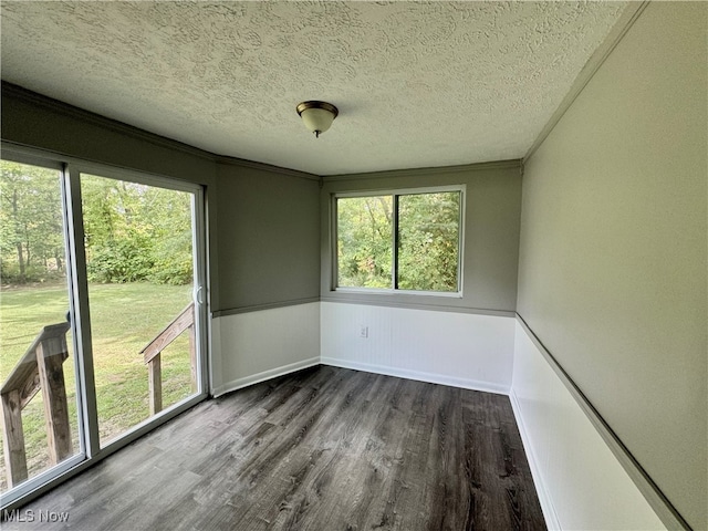 empty room with a textured ceiling, dark hardwood / wood-style floors, and crown molding