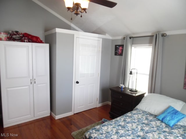 bedroom with a closet, dark wood-type flooring, vaulted ceiling, ornamental molding, and ceiling fan