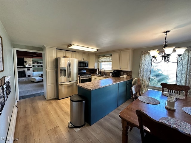 kitchen with pendant lighting, a notable chandelier, kitchen peninsula, light hardwood / wood-style flooring, and appliances with stainless steel finishes