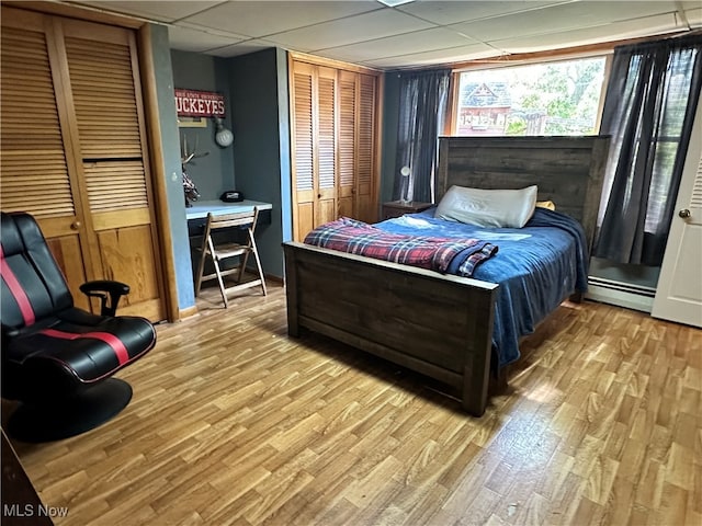 bedroom featuring a drop ceiling, a baseboard heating unit, and light wood-type flooring