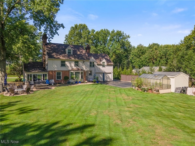 back of property with a garage, a lawn, a patio, and an outbuilding