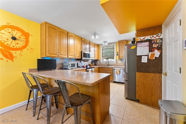 kitchen featuring sink, kitchen peninsula, a kitchen breakfast bar, appliances with stainless steel finishes, and light tile patterned floors